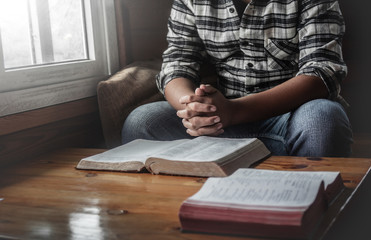 Young male praying with open bible on wooden table at home