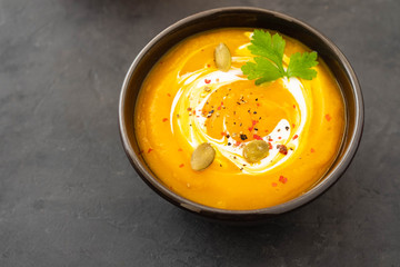 Pumpkin soup in a bowl with fresh pumpkins, garlic and parsley herbs on a black background. Autumn...