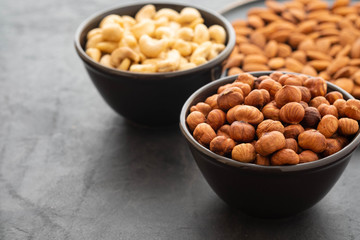 Assorted nuts in bowls on a black background. Copy space.