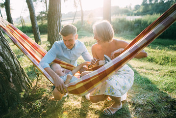 Young sympathetic family - mom, dad and son rest in the nature, sitting in a hammock