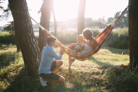 Young sympathetic family - mom, dad and son rest in the nature, sitting in a hammock - Powered by Adobe