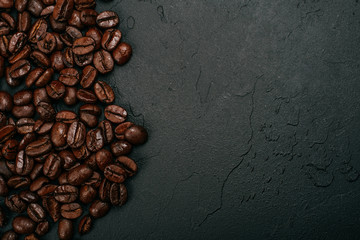 Roasted brown coffee beans on the black concrete stone background. Flatlay style, messy pattern.