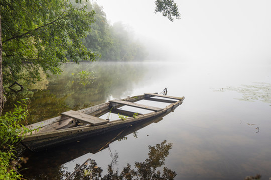 Fog, mist or haze over a lake and a fishing boot. Colorful leaves and foggy skies with some white clouds. Masuria region, Poland.