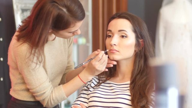 Wedding makeup for a young bride - in salon applying lipstick pencil