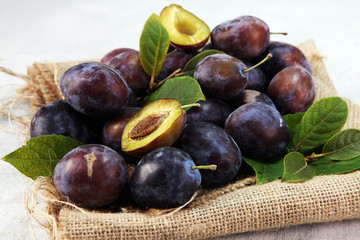 Plums on rustic background. Half of blue plum fruit. Many beautiful plums with leaves