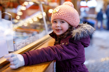 Little cute kid girl near sweet stand with sugared apples and chocolate fruits. Happy child on...