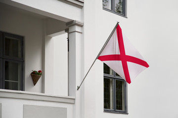 Alabama flag. Alabama flag hanging on a pole in front of the house. National flag waving on a home displaying on a pole on a front door of a building. Flag raised at a full staff.