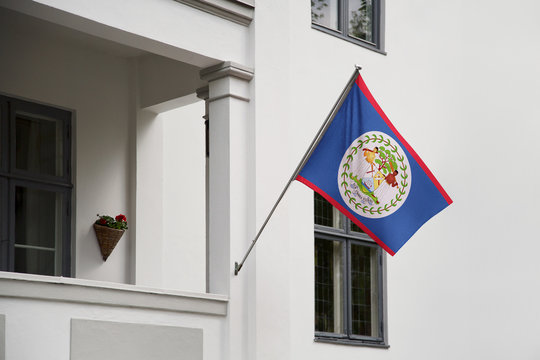 Belize flag. Belize flag hanging on a pole in front of the house. National flag of waving on a home displaying on a pole on a front door of a building. Flag raised at a full staff.