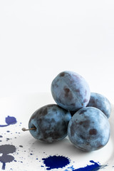Big, juicy, blue plums on a plate in the blots. White background.  Place for text.