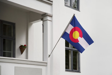 Colorado flag.  Colorado state flag hanging on a pole in front of the house. State flag waving on a home displaying on a pole on a front door of a building.Flag raised at a full staff.