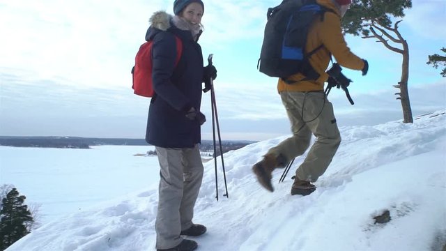 Group of young people hiking in mountains in winter. Backpackers walking on snow in Scandinavia, help each other, take pictures and enjoy nature. Slow motion
