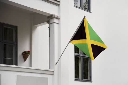 Jamaica flag. Jamaica flag hanging on a pole in front of the house. National flag of waving on a home displaying on a pole on a front door of a building. Flag raised at a full staff.