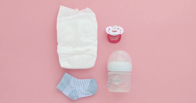 Set for a newborn nipple bottle diaper socks pink background top view