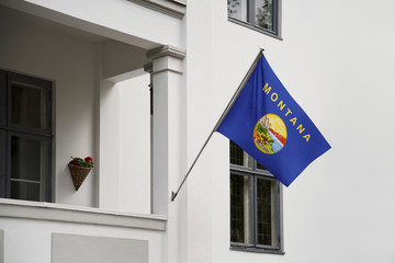 Montana flag.  Montana state flag hanging on a pole in front of the house. State flag waving on a home displaying on a pole on a front door of a building.Flag raised at a full staff. - 221949313