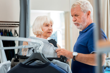 Fototapeta premium I doubt. Enthusiastic wonderful elderly wife suggesting a pullover while her husband expressing hesitation concerning a purchase