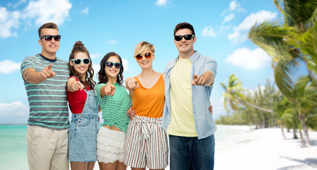 friendship, travel, tourism and summer holidays concept - group of happy smiling friends in sunglasses pointing finger at you over tropical beach background in french polynesia