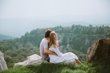 Young couple sitting on the edge of mountains with a beautiful view