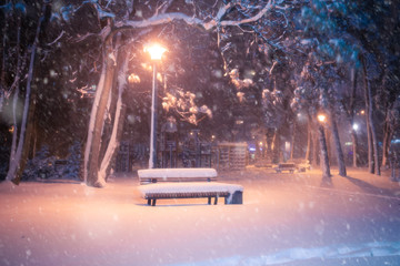 Nachtwinterlandschaft mit Schneefall. Verschneite Gasse des beleuchteten Parks der Stadt