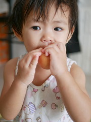 Little Asian baby girl eating eggshell, not knowing that she has to peel the egg before eating it - baby taking eggshell that is not well grounded and cleaned up may cause injury and infection