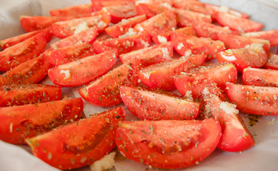 The manufacturing process of sundried tomatoes cut into slices sprinkled with salt, oregano, Basil, thyme being dried out in the sun or in the oven Close-up, selective focus.