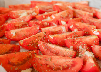 The manufacturing process of sundried tomatoes cut into slices sprinkled with salt, oregano, Basil, thyme being dried out in the sun or in the oven Close-up, selective focus.