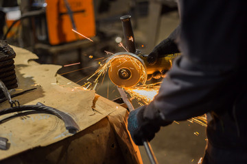 Professional blacksmith sawing metal with hand circular saw at forge, workshop. Handmade,...