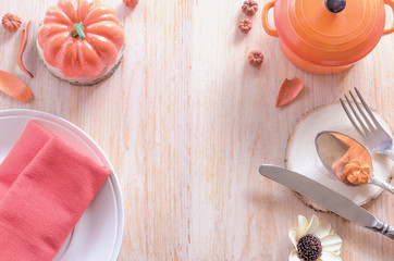 Thanksgiving table settings, dinner plate and cutlery, pot of pumpkin soup and traditional pumpkin and autumn dry leaves on wood background. Happy Thanksgiving Day concept. Copy space.