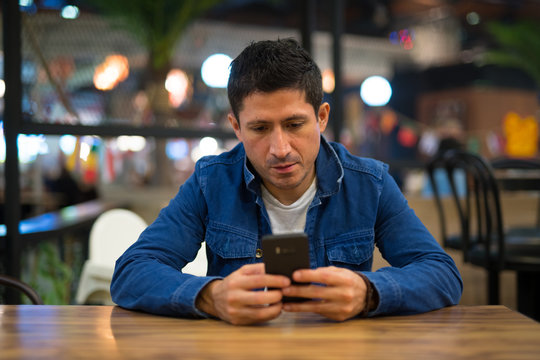 Hispanic Man Relaxing Using Phone At The Restaurant