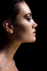 Fototapeta premium profile portrait of attractive glamorous woman posing with makeup and glitter on body, isolated on black