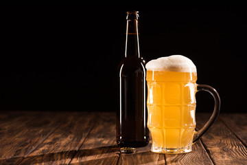 bottle of beer and mug of fresh light beer with foam at wooden table, minimalistic concept