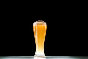 glass of fresh beer with foam at table on black background, minimalistic concept
