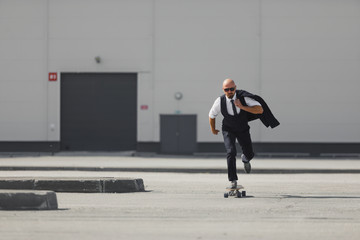 Confident young businessman in business suit on longboard hurrying to his office, on the street in the city