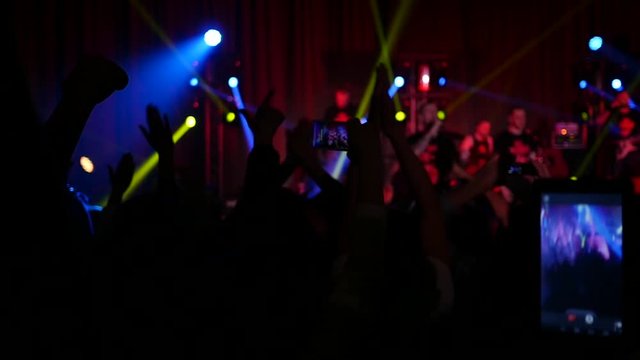Cheering crowd fan spectators silhouettes rais hands phones at concert lumiere