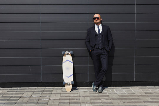 Fashionable business man in perfect suite on the street, using skateboard longboard and sute man
