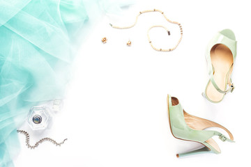 Woman's accessories on white table, top view, flat lay. Female workspace with turquoise shoes and full ballerina skirt, pearl necklace, bottle of perfume. Copy space for your text