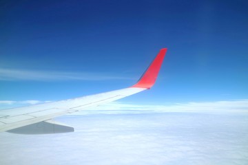 Beautiful view from airplane's window with airplane's wing, blue sky and white cloud in the summer morning. Soft focus.