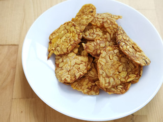 Fried tempeh in a white plate on the wooden surface. 