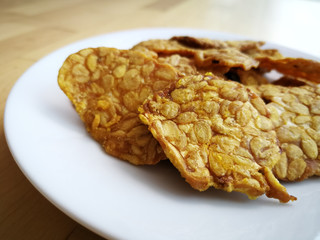 Fried tempeh in a white plate on the wooden surface. 