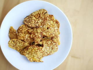 Fried tempeh in a white plate on the wooden surface. 