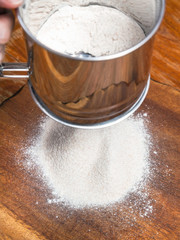 sifting the flour through steel sieve on board