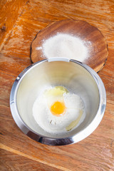flour with broken egg in steel bowl and board