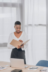 stylish attractive african american businesswoman looking in folder in office