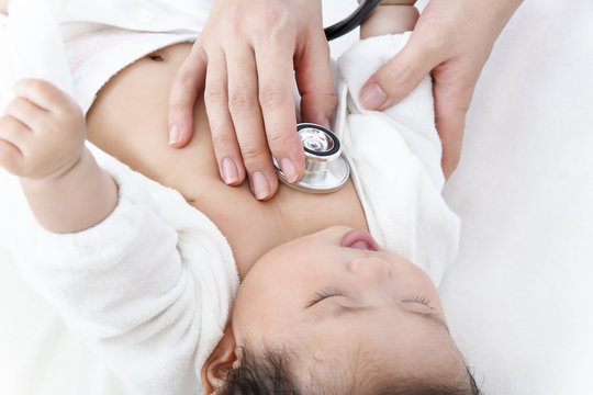 病院で胸に聴診器を当て診察を受ける新生児の赤ちゃん。子供の健康診断、健診,定期健診,診察,病気イメージ