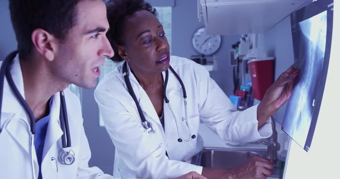 Senior African radiologist consulting with young Hispanic colleague over patient x rays. Two medical doctors reviewing patient x-ray of patients spine and skull