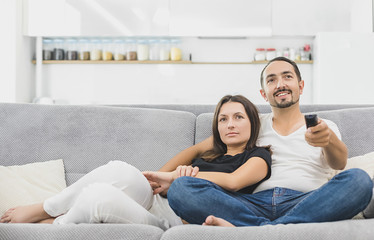 Obraz premium Happy Young Couple In Livingroom Sitting On Couch Watching Movie