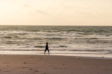 Fototapeta na wymiar 朝焼けの海岸を歩く女性 / リラックスイメージ