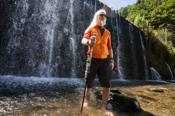 Men with a hiking stick standing in front of a waterfall