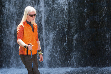 Men with a long blonde hair standing in nature in front of a waterfall