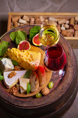 Red and white wine with cheese, grapes, figs and nuts on old cask in wine cellar. Glasses and bottles of wine. View from above, top studio shot