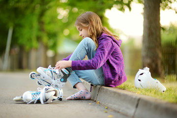 Pretty little girl learning to roller skate on summer day in a park. Child wearing safety helmet enjoying roller skating ride outdoors.